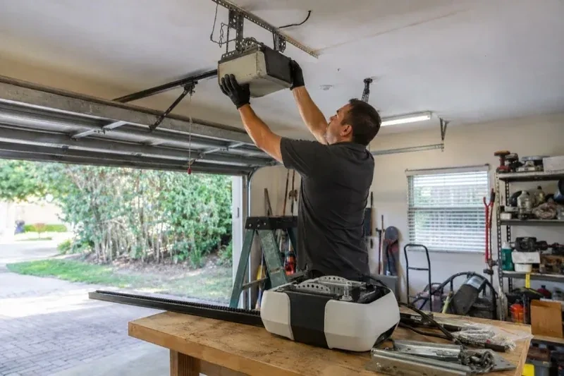 Person holding an overhead garage-door opener beside another opener and hardware on a workbench — Garage Door Opener Replacement, Hamilton