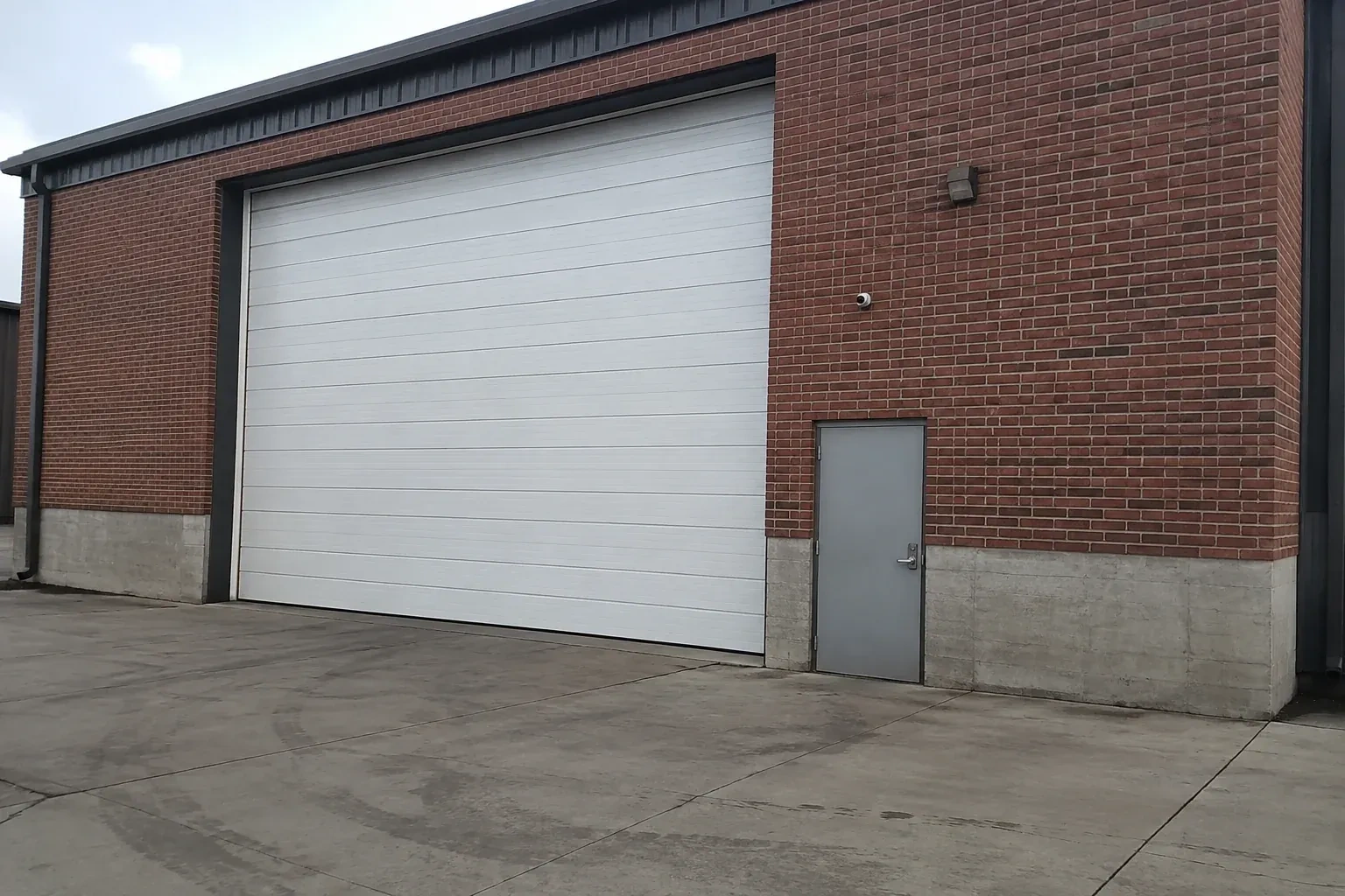 Tall closed sectional loading door beside a personnel door at a brick unit. — Commercial Sectional Door Repair, Hamilton
